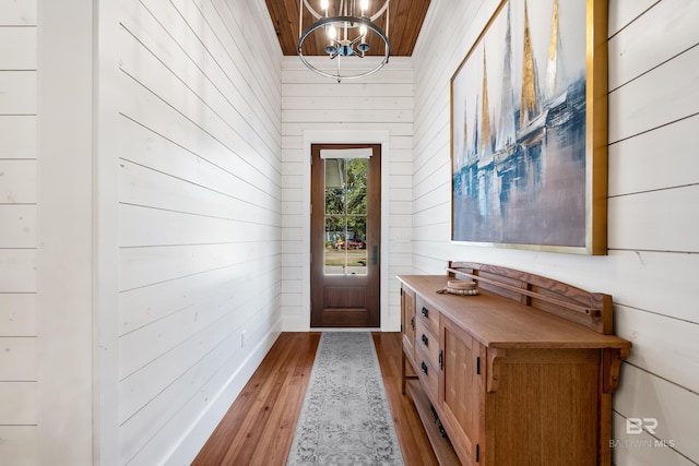 doorway featuring a chandelier, wood ceiling, wooden walls, and wood finished floors