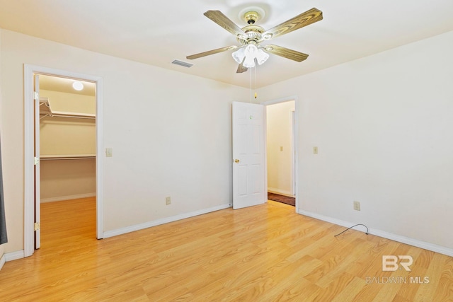 unfurnished bedroom with a closet, light wood-type flooring, a walk in closet, and ceiling fan