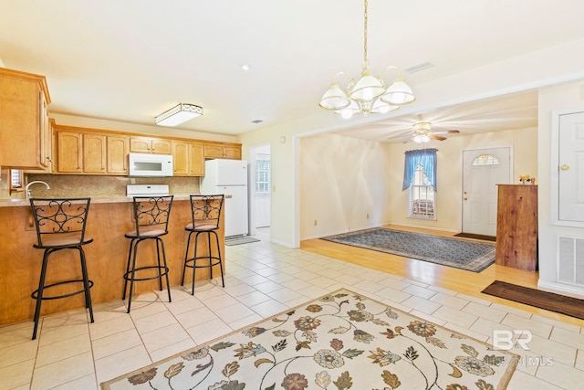 kitchen with ceiling fan with notable chandelier, decorative backsplash, a breakfast bar area, light wood-type flooring, and white appliances