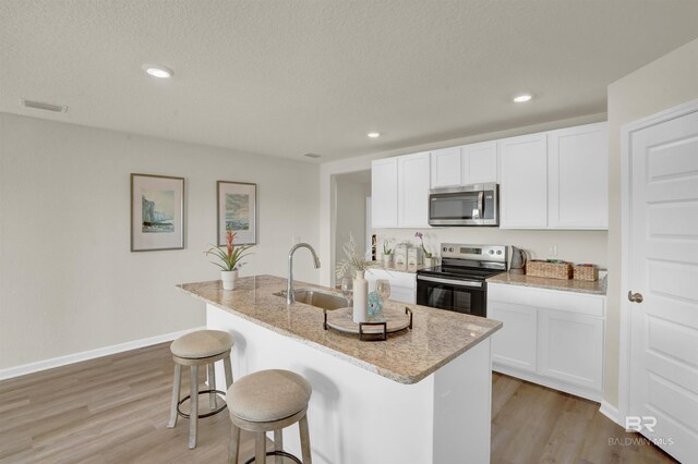 kitchen featuring a sink, a breakfast bar, appliances with stainless steel finishes, a center island with sink, and visible vents