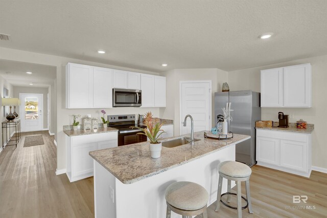 kitchen with white cabinets, light wood finished floors, stainless steel appliances, a sink, and light stone counters