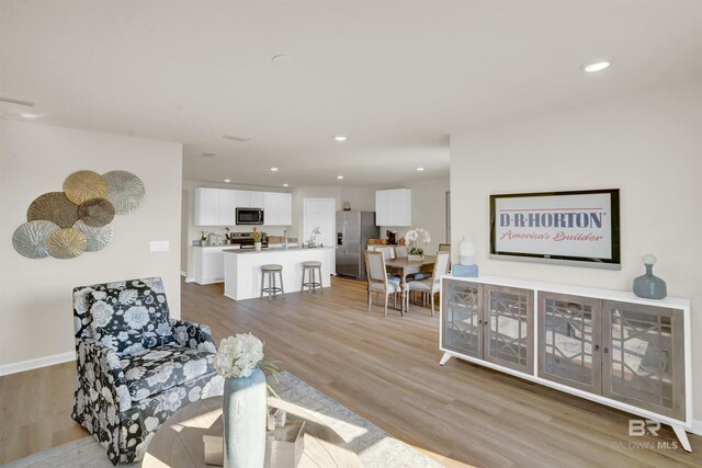 living area with baseboards, light wood-style flooring, and recessed lighting