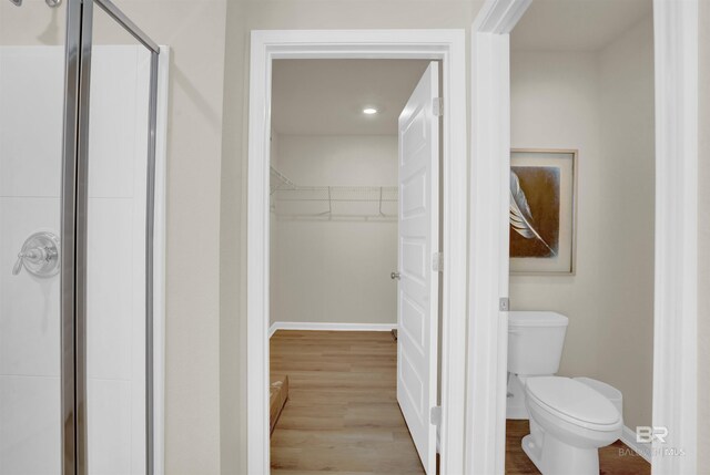 bathroom featuring a spacious closet, wood finished floors, baseboards, and a shower stall