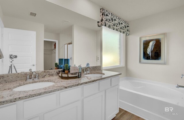 bathroom with double vanity, visible vents, a sink, and a garden tub