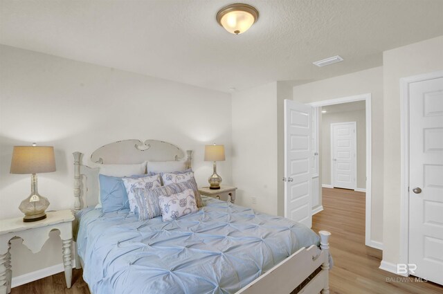 bedroom with baseboards, visible vents, and wood finished floors