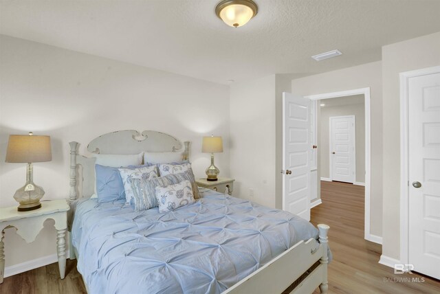 bedroom featuring baseboards, visible vents, wood finished floors, and a textured ceiling