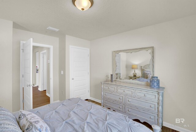 bedroom featuring wood finished floors, a textured ceiling, baseboards, and visible vents