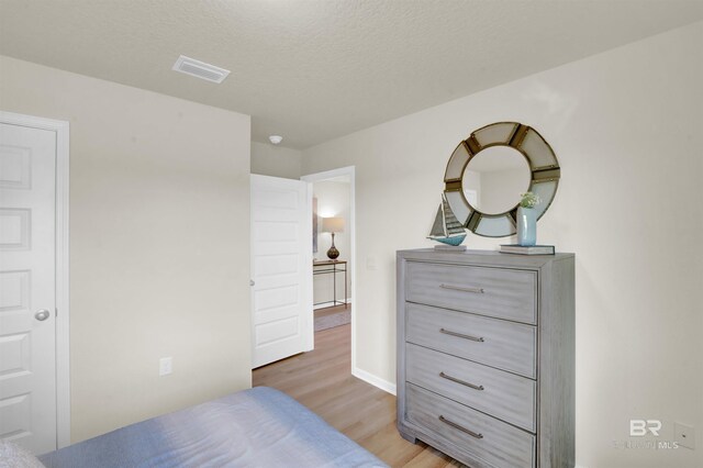 bedroom with a textured ceiling, light wood-style floors, and visible vents