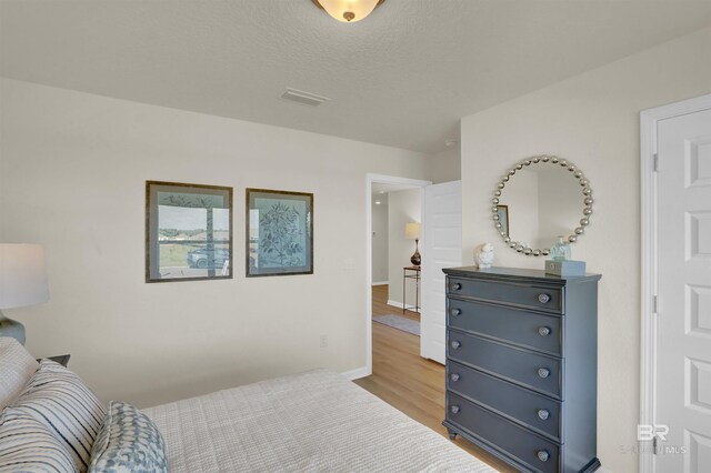 bedroom with visible vents, a textured ceiling, baseboards, and light wood-type flooring