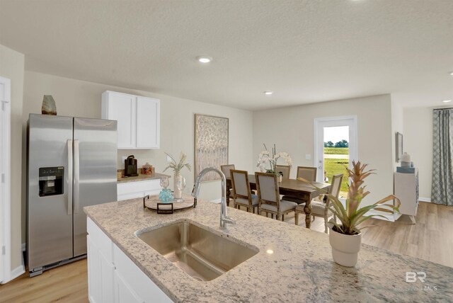 kitchen with white cabinets, light stone countertops, a sink, stainless steel refrigerator with ice dispenser, and light wood-type flooring