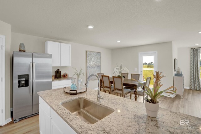 kitchen featuring white cabinetry, stainless steel fridge, light wood-type flooring, a sink, and light stone counters