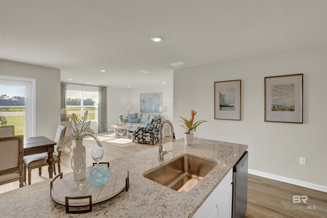 kitchen with open floor plan, a sink, wood finished floors, and light stone counters