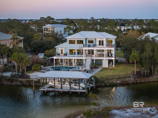 30471 Harbour Dr, Orange Beach, AL 36561 - back of property at dusk with a balcony, a fenced backyard, a water view, a patio area, and a lawn