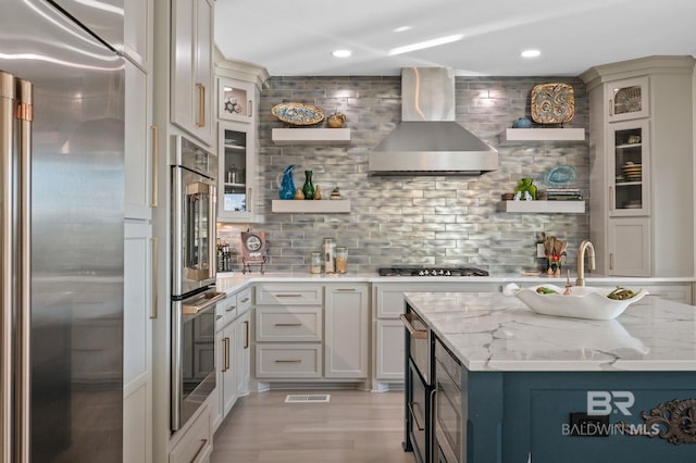 30471 Harbour Dr, Orange Beach, AL 36561 - kitchen featuring appliances with stainless steel finishes, wall chimney exhaust hood, light wood finished floors, decorative backsplash, and light stone countertops