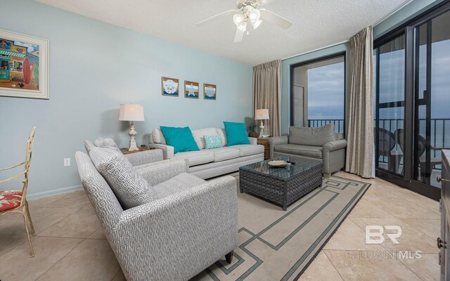 living area featuring ceiling fan, a textured ceiling, light tile patterned flooring, and baseboards