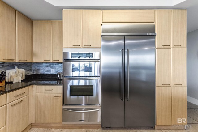 28105 Perdido Beach Blvd Unit C-314, Orange Beach, AL 36561 - kitchen with light brown cabinetry, appliances with stainless steel finishes, dark stone countertops, decorative backsplash, and a warming drawer