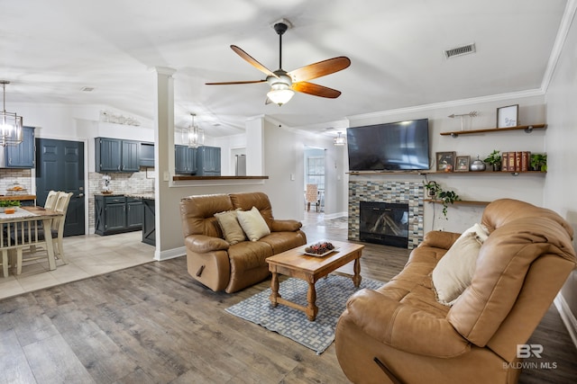 living room featuring ornamental molding, a fireplace, ceiling fan, and light hardwood / wood-style flooring