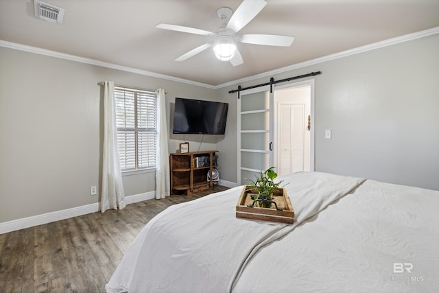 bedroom featuring ornamental molding, a barn door, ceiling fan, and wood-type flooring