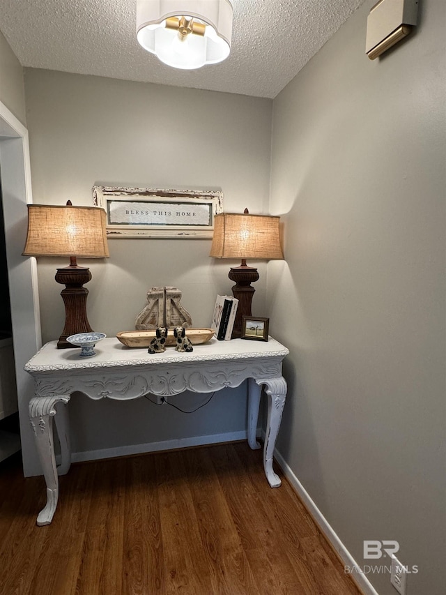 interior space featuring a textured ceiling, baseboards, wood finished floors, and a wall mounted AC