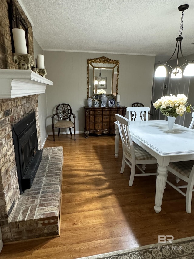 dining area featuring an inviting chandelier, ornamental molding, a brick fireplace, a textured ceiling, and wood finished floors