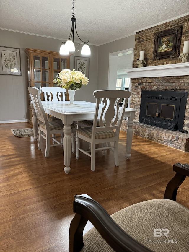 dining room with a textured ceiling, a brick fireplace, wood finished floors, and crown molding