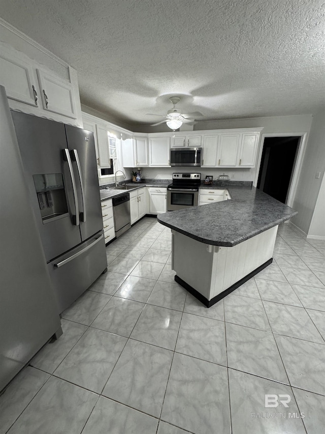 kitchen featuring a ceiling fan, dark countertops, appliances with stainless steel finishes, white cabinetry, and a sink