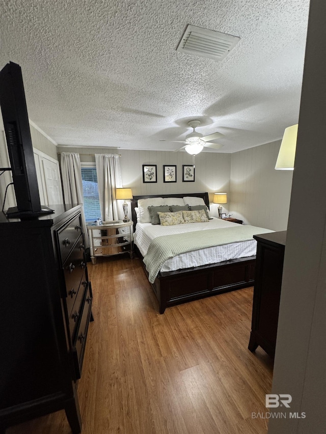 bedroom featuring visible vents, ceiling fan, wood finished floors, a wood stove, and a textured ceiling