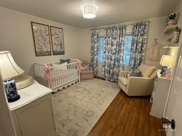 bedroom featuring a nursery area, a textured ceiling, and wood finished floors