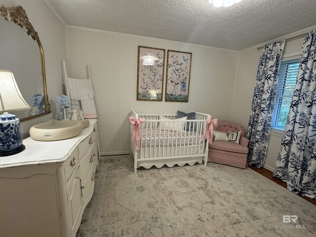 bedroom featuring ornamental molding, a crib, and a textured ceiling