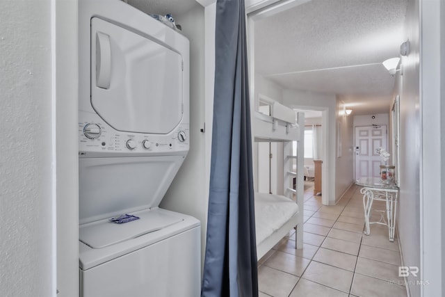 laundry area featuring stacked washer and clothes dryer, light tile patterned floors, a textured ceiling, and laundry area