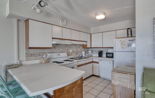 kitchen featuring white appliances, a peninsula, light countertops, under cabinet range hood, and a sink