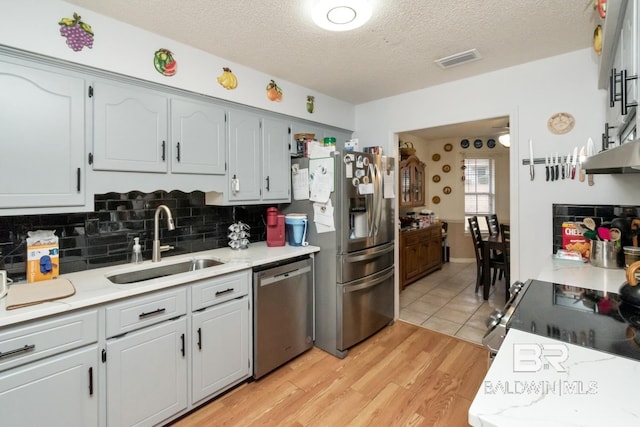 kitchen with sink, appliances with stainless steel finishes, tasteful backsplash, a textured ceiling, and light wood-type flooring