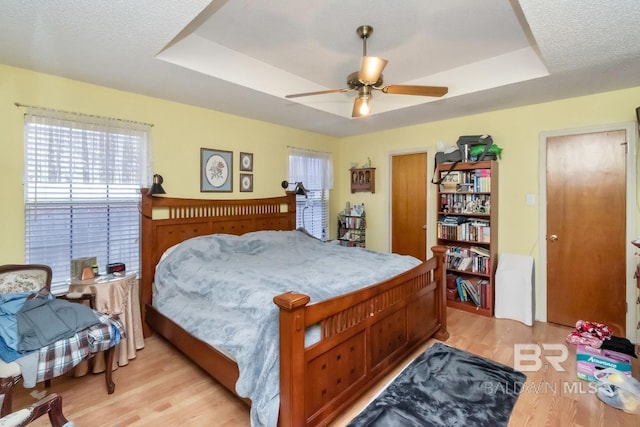 bedroom with ceiling fan, a tray ceiling, light hardwood / wood-style flooring, and a textured ceiling