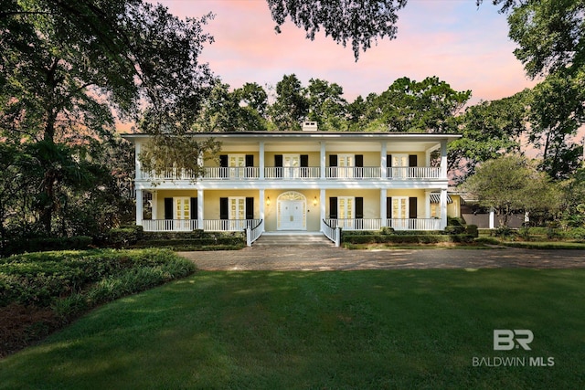 neoclassical / greek revival house with a balcony, covered porch, and a lawn