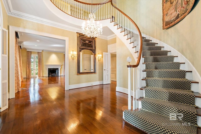 stairs featuring an inviting chandelier, crown molding, a towering ceiling, a fireplace, and hardwood / wood-style flooring