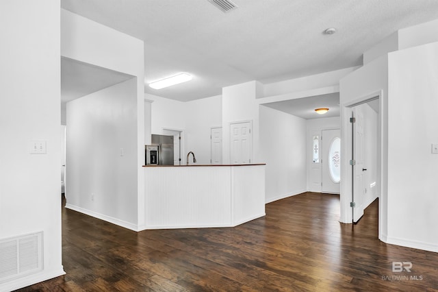 interior space with dark wood-style floors, a sink, dark countertops, visible vents, and stainless steel refrigerator with ice dispenser