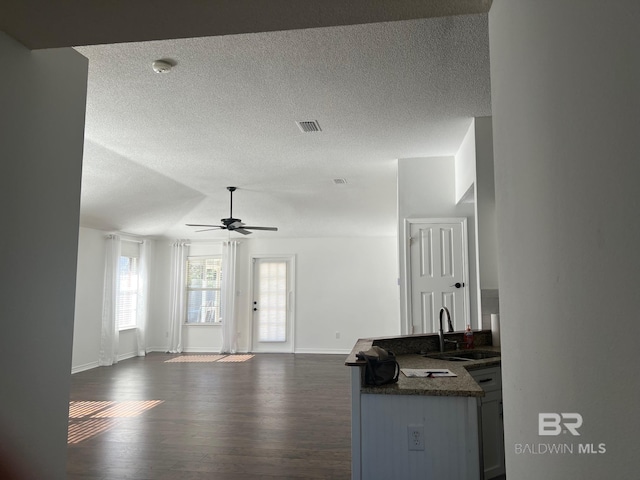 living area featuring a textured ceiling, visible vents, baseboards, a ceiling fan, and dark wood-type flooring