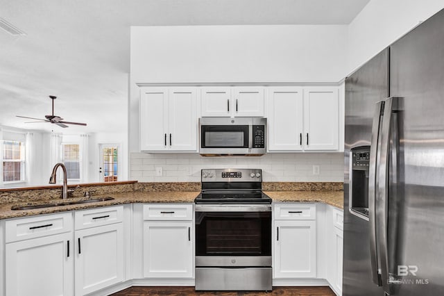 kitchen with white cabinets, stainless steel appliances, a sink, stone counters, and tasteful backsplash