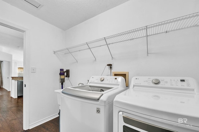 clothes washing area featuring laundry area, washing machine and clothes dryer, baseboards, a textured ceiling, and dark wood-style flooring