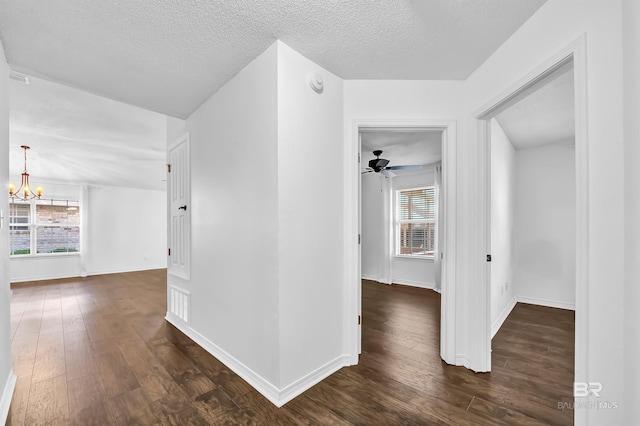 corridor with dark wood finished floors, a healthy amount of sunlight, baseboards, and a notable chandelier