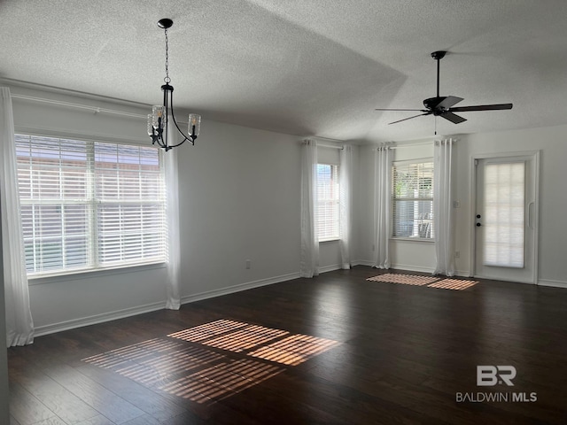 unfurnished dining area featuring dark wood finished floors, baseboards, a textured ceiling, and ceiling fan with notable chandelier