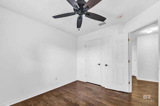 unfurnished bedroom featuring dark wood-style flooring, baseboards, visible vents, a closet, and ceiling fan