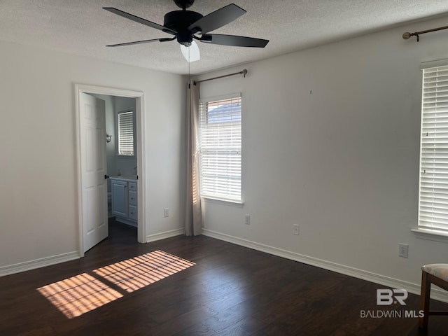 unfurnished bedroom with a textured ceiling, dark wood-style flooring, ensuite bathroom, baseboards, and a ceiling fan