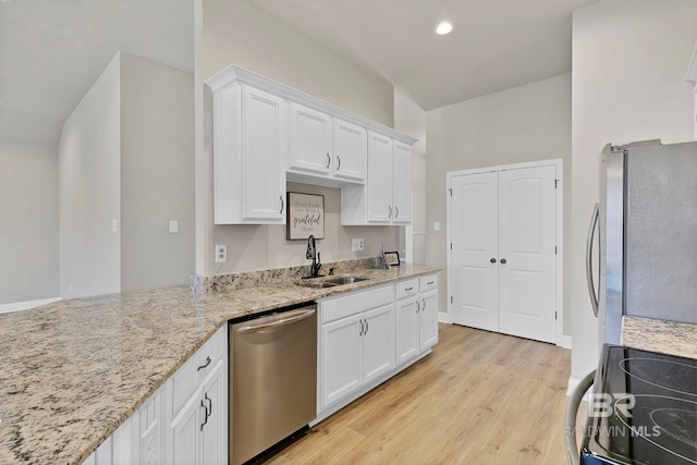 kitchen with a sink, stainless steel appliances, light wood finished floors, white cabinets, and light stone countertops