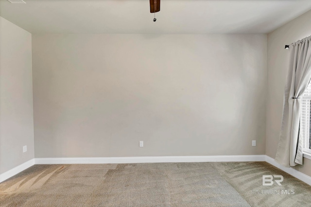 carpeted spare room featuring baseboards and a ceiling fan