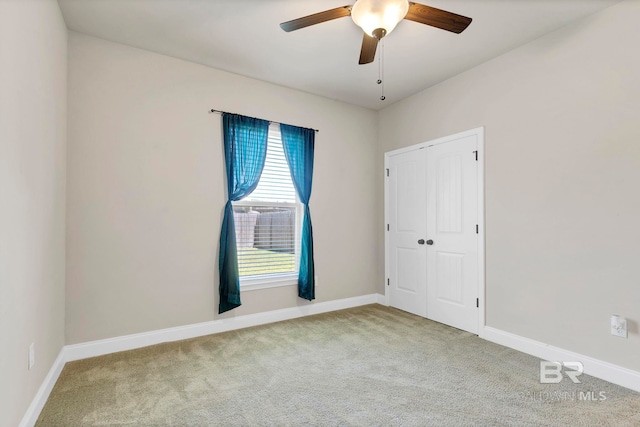 carpeted spare room featuring baseboards and a ceiling fan