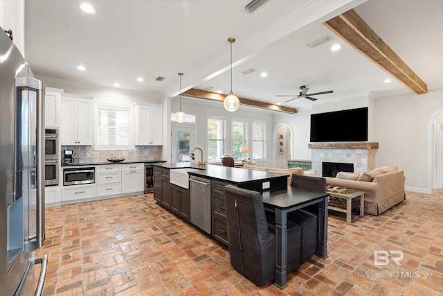 kitchen with hanging light fixtures, appliances with stainless steel finishes, a center island with sink, and white cabinets