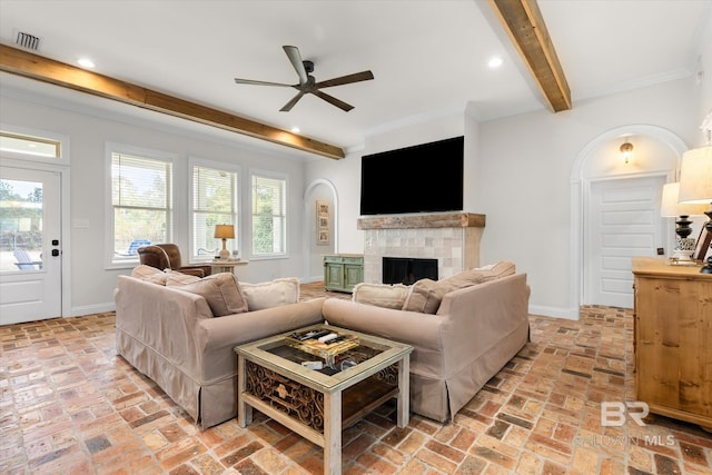 living room with beamed ceiling, a tiled fireplace, and ceiling fan