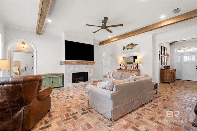 living room with beamed ceiling, a tile fireplace, and ceiling fan