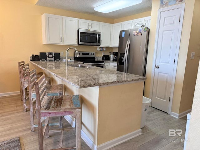 kitchen with light hardwood / wood-style floors, appliances with stainless steel finishes, kitchen peninsula, and white cabinets